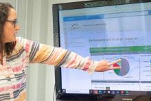 A person pointing to a monitor explaining a visual dashboard.