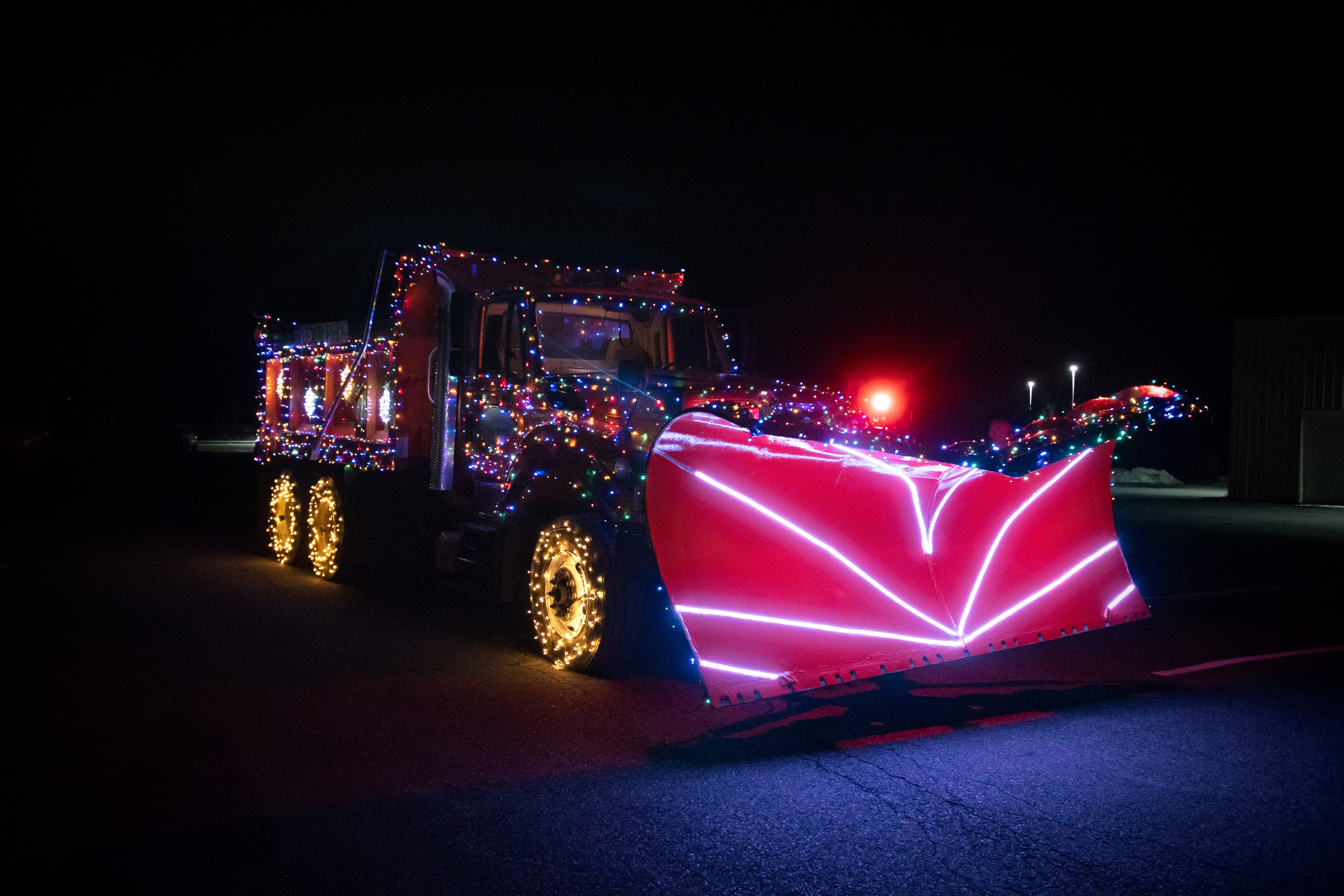 A front view of Rudolph the Holiday Snowplow featuring a prominent red light for a nose and a plow blade lined with white lights.