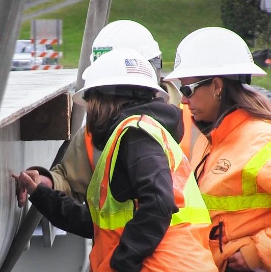 Three workers in hard hats point to a bridge beam