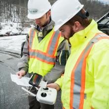 Two men in hardhats and reflective gear looking at a piece of paper.